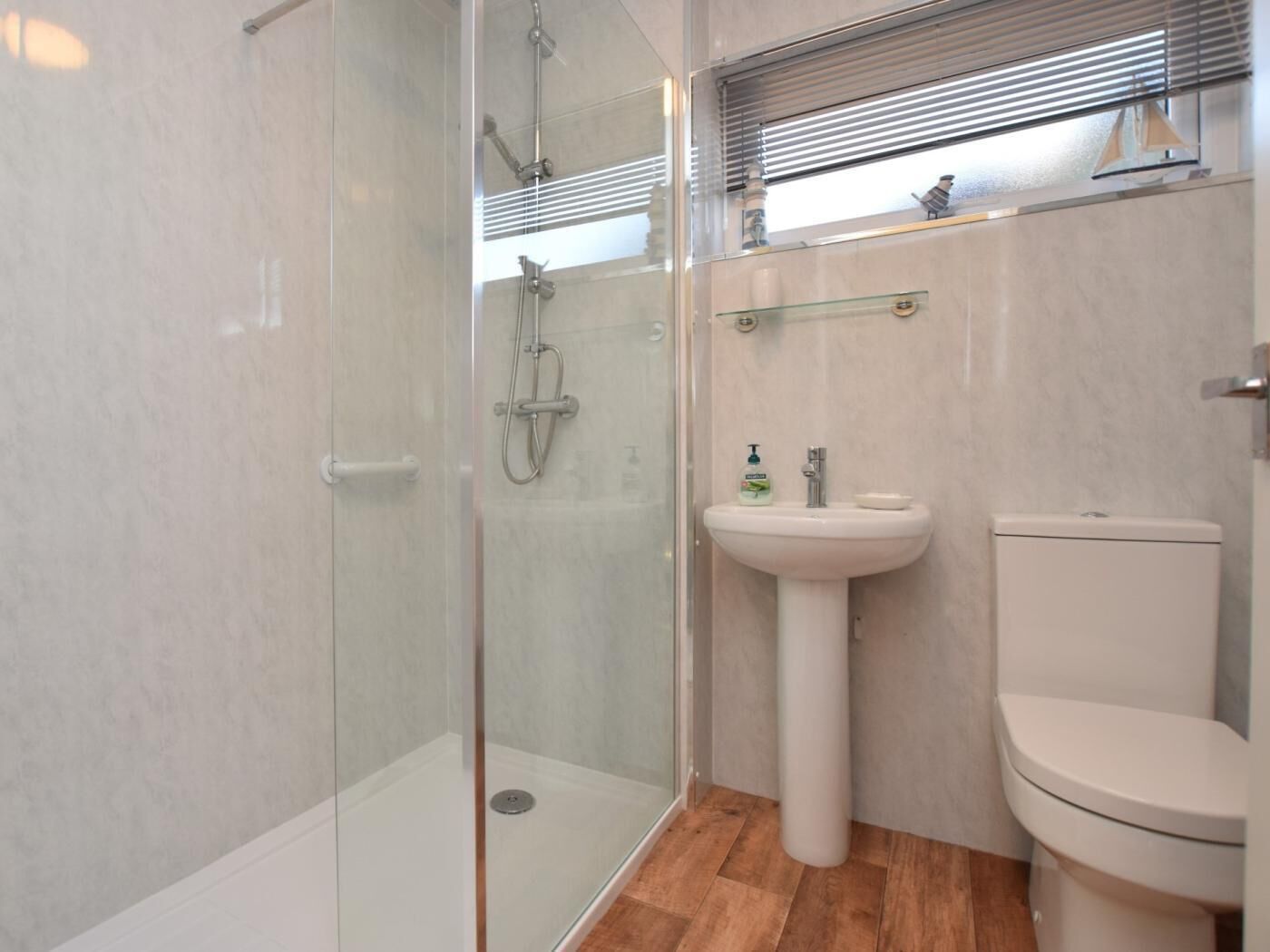 A bathroom with a glass-enclosed shower, a pedestal sink, and a toilet.