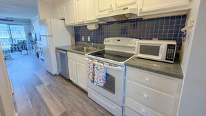 A kitchen with white cabinets, a stove, a microwave, and a sink. - Ocean view, steps to beach with a relaxing pool! (Ocean City)
