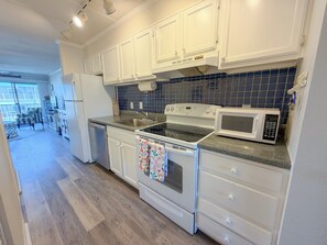 A kitchen with white cabinets, a stove, a microwave, and a sink. - Ocean view, steps to beach with a relaxing pool! (Ocean City)