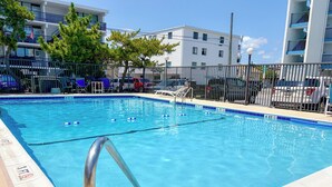 A clear swimming pool with a metal ladder, surrounded by a fence, and buildings in the background. - Ocean view, steps to beach with a relaxing pool! (Ocean City)