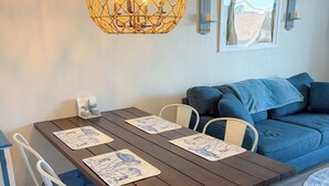 A dining area with a wooden table, white chairs, and a hanging light fixture. - Ocean view, steps to beach with a relaxing pool! (Ocean City)