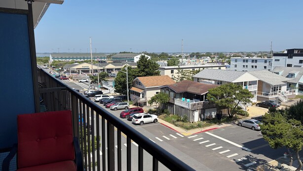 A balcony with a red chair, a view of a parking lot with cars, and buildings in the background. - Ocean view, steps to beach with a relaxing pool! (Ocean City)