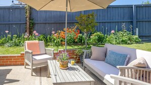 Eine Außenpatio mit Holztisch, zwei Stühlen, einer Couch und einem großen Sonnenschirm.
