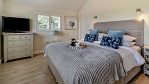 Un dormitorio con cama, televisor en una cómoda, ventana y mesita de noche.