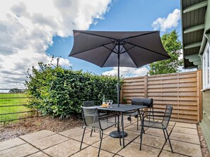 Een terras buiten met een tafel, stoelen, een grote parasol en een houten omheining.
