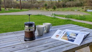 Ein Holztisch mit einer French-Press-Kaffeemaschine, zwei weißen Tassen und einer Zeitung.