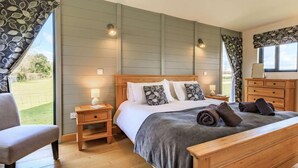Ein Schlafzimmer mit einem hölzernen Bett, Nachttischen, einem Sessel und Blick ins Freie.