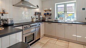 Een moderne keuken met witte kasten, een roestvrijstalen afzuigkap, een ingebouwde oven en een raam met uitzicht op buiten.