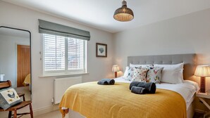 Een slaapkamer met een bed, bedlampen, een raam met jaloezieën, een stoel en een nachtkastje.