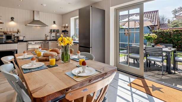 Een moderne keuken met witte kasten, een eethoek met een houten tafel en uitzicht op de achtertuin.