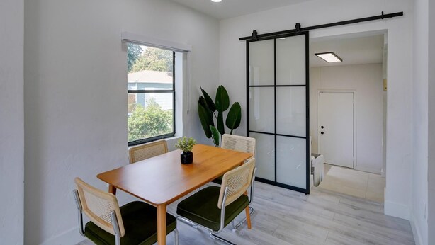 A modern room with a wooden table, four chairs, a large plant, a sliding glass door, and a view of the outside. - 1935 NW 42nd St. (Miami)
