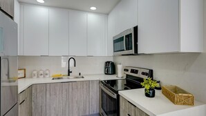 A modern kitchen with white cabinets, a stainless steel stove, a microwave, and a sink. - 1935 NW 42nd St. (Miami)