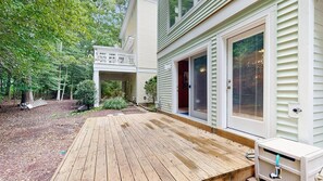 Une terrasse en bois menant à une maison dotée d’un porche couvert et d’une porte-fenêtre coulissante.