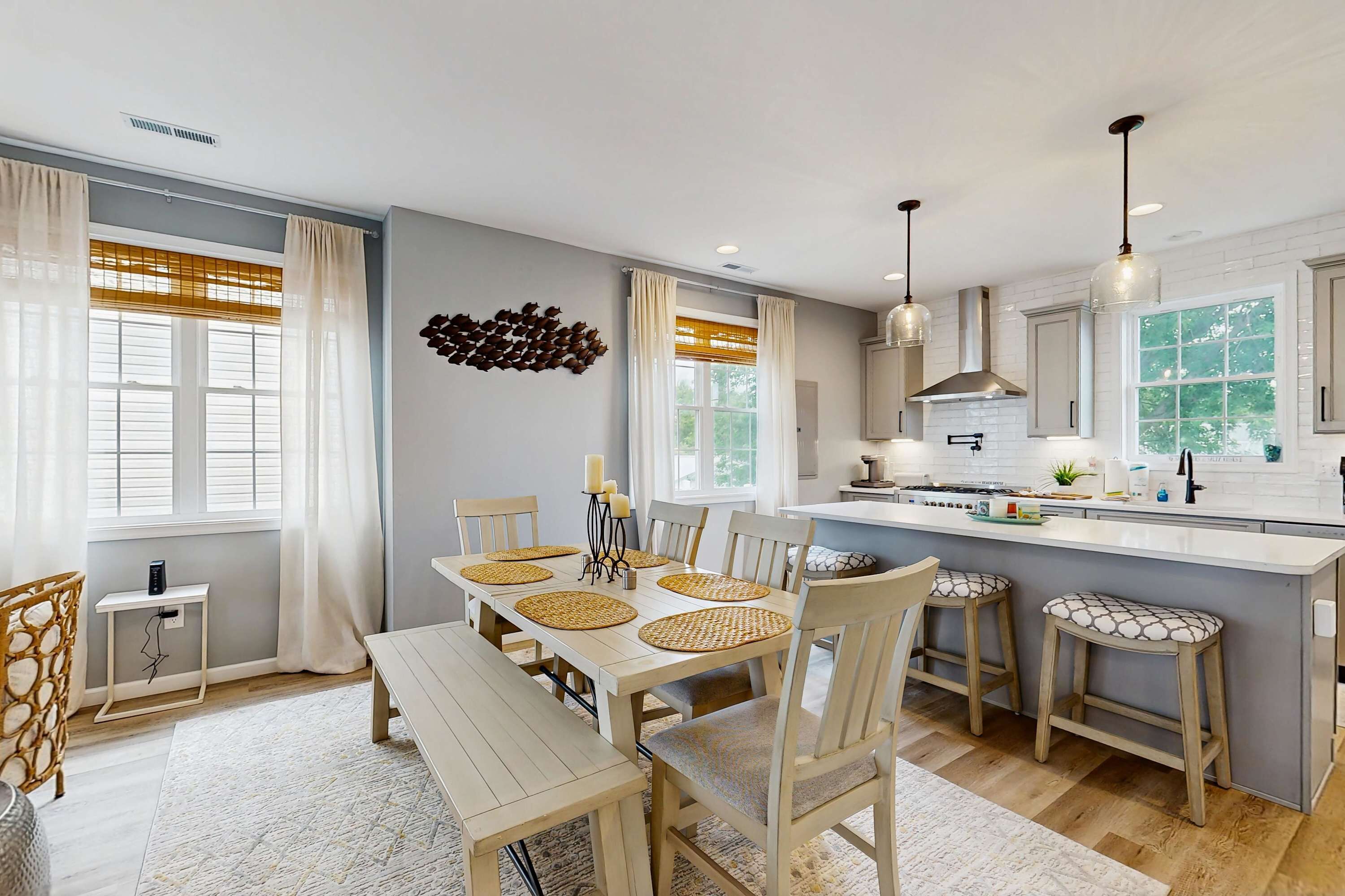 A modern kitchen with a central island, bar stools, and a dining table set for six.