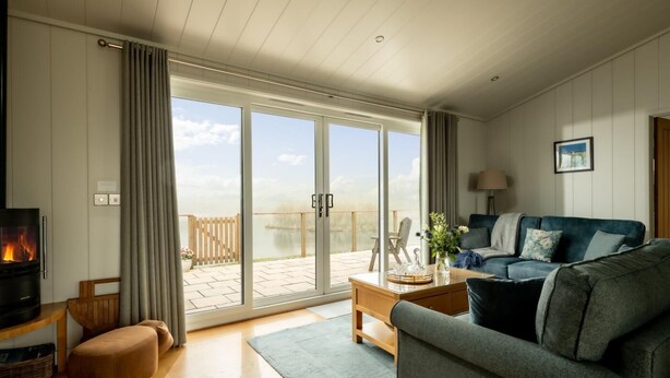 Een woonkamer met een bank, een salontafel, een open haard en uitzicht op een meer door grote schuifdeuren.