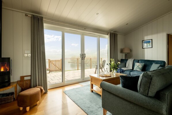 A living room with a sofa, a coffee table, a fireplace, and a view of a lake through large sliding doors.