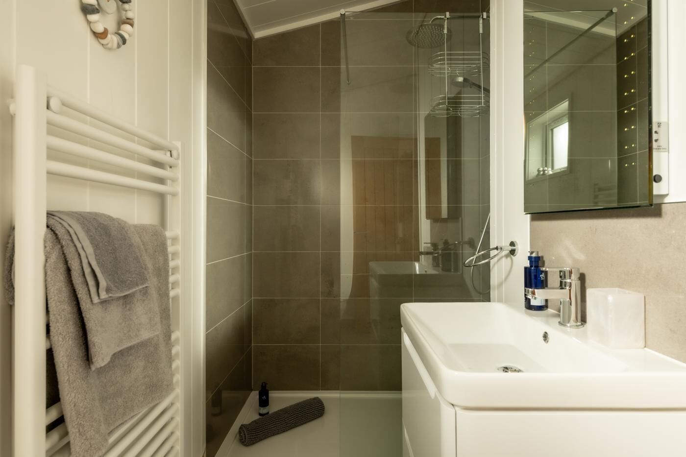 Un bagno con un lavandino bianco, un portascopevoli, una doccia con porta in vetro e uno specchio sopra il lavandino.