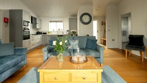 Een moderne woonkamer met een bank, een bijzettafeltje met bloemen, en een keuken op de achtergrond.