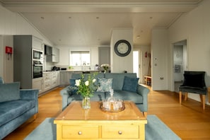 A modern living room with a sofa, a coffee table with flowers, and a kitchen in the background.