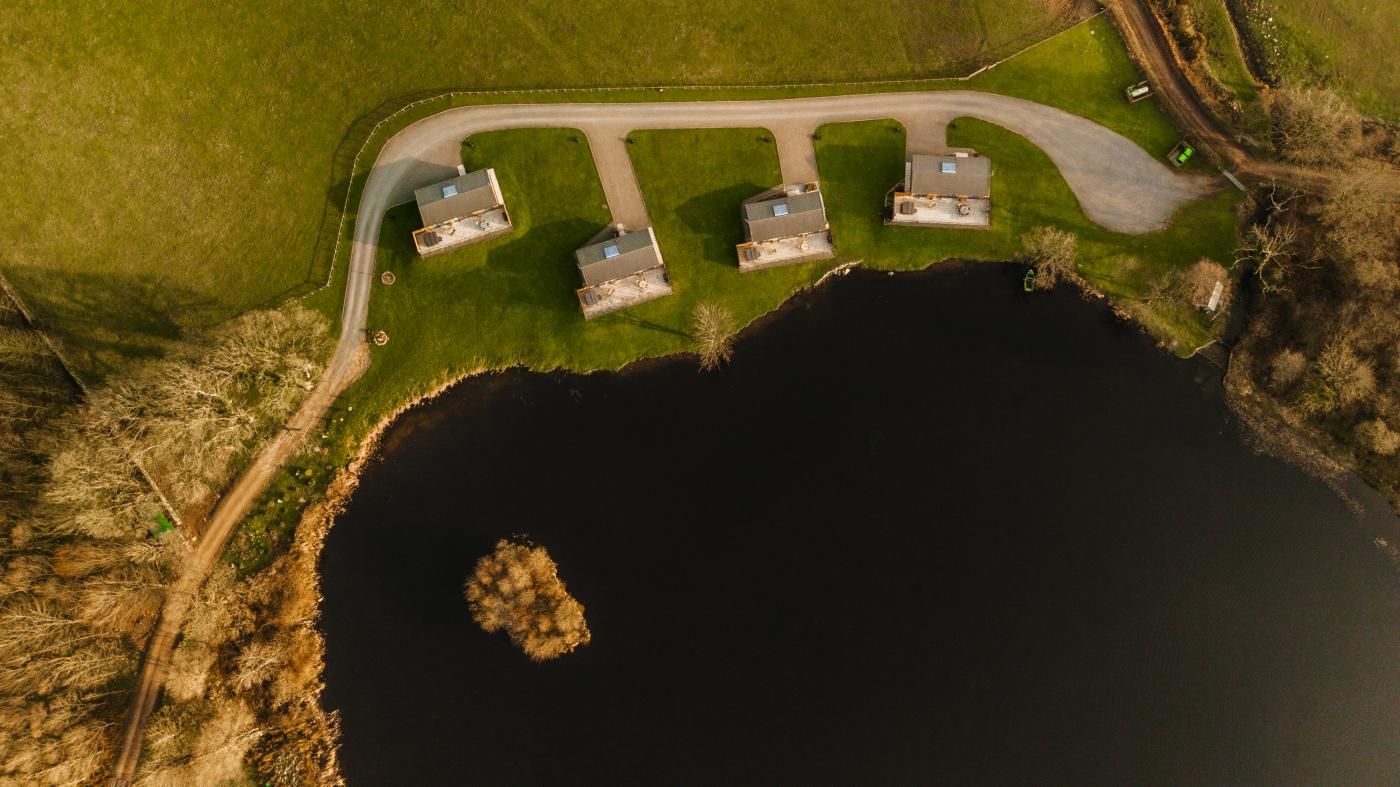 Ett flygbildsfoto av en fastighet med en sjö, tre byggnader och en svängd uppfart.