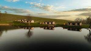 Een landgoed aan het meer met meerdere gebouwen, een grasheuvel en schapen op de achtergrond.