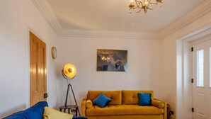 Een woonkamer met een blauwe bank, een mosterdgele bank, een vloerlamp en een kroonluchter.