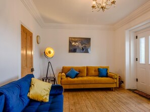 A living room with a blue sofa, a mustard-colored sofa, a floor lamp, and a chandelier. - 2 Bed in Norwich (oc-78491) (Bacton)