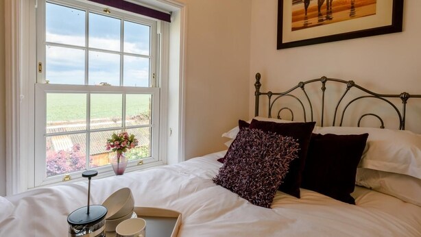 Een slaapkamer met een groot raam, een bed met wit beddengoed, een metalen hoofdeinde en een ingelijste foto aan de muur.