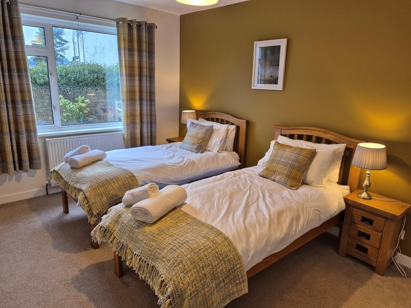 A double room with two beds, a bedside table with a lamp, a radiator, and a window with curtains.