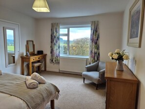 A bedroom with a bed, a desk, a chair, a radiator, a window with curtains, and a vase with flowers. - 3 Bed in Dumfries (oc-77430) (Auldgirth)