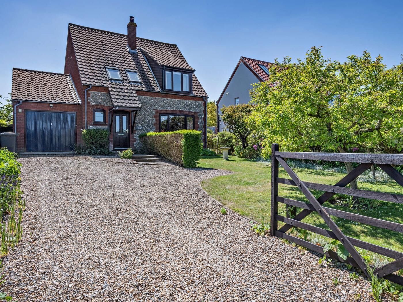 A house with a gravel driveway, a wooden gate, and a well-maintained garden.