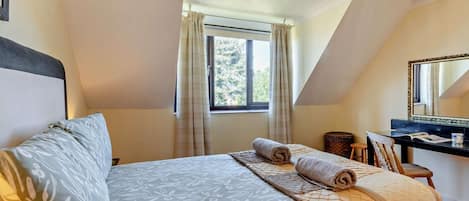 Quarto com cama, escrivaninha, cadeira, janela com cortinas e espelho na parede.