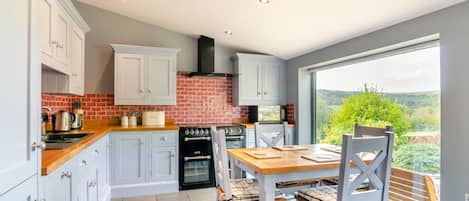 A modern kitchen with white cabinets, a brick backsplash, and a view of the countryside through large windows.