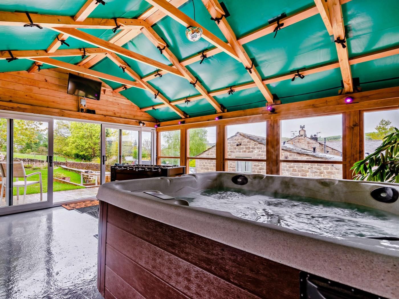 A spa area with a hot tub, wooden ceiling, and large windows offering a view of the surrounding landscape.