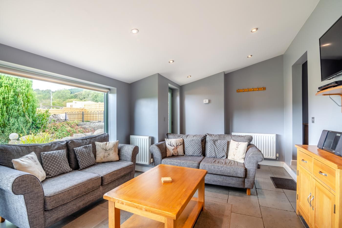 A modern living room with a grey sofa set, a wooden coffee table, and a TV on a wooden stand.