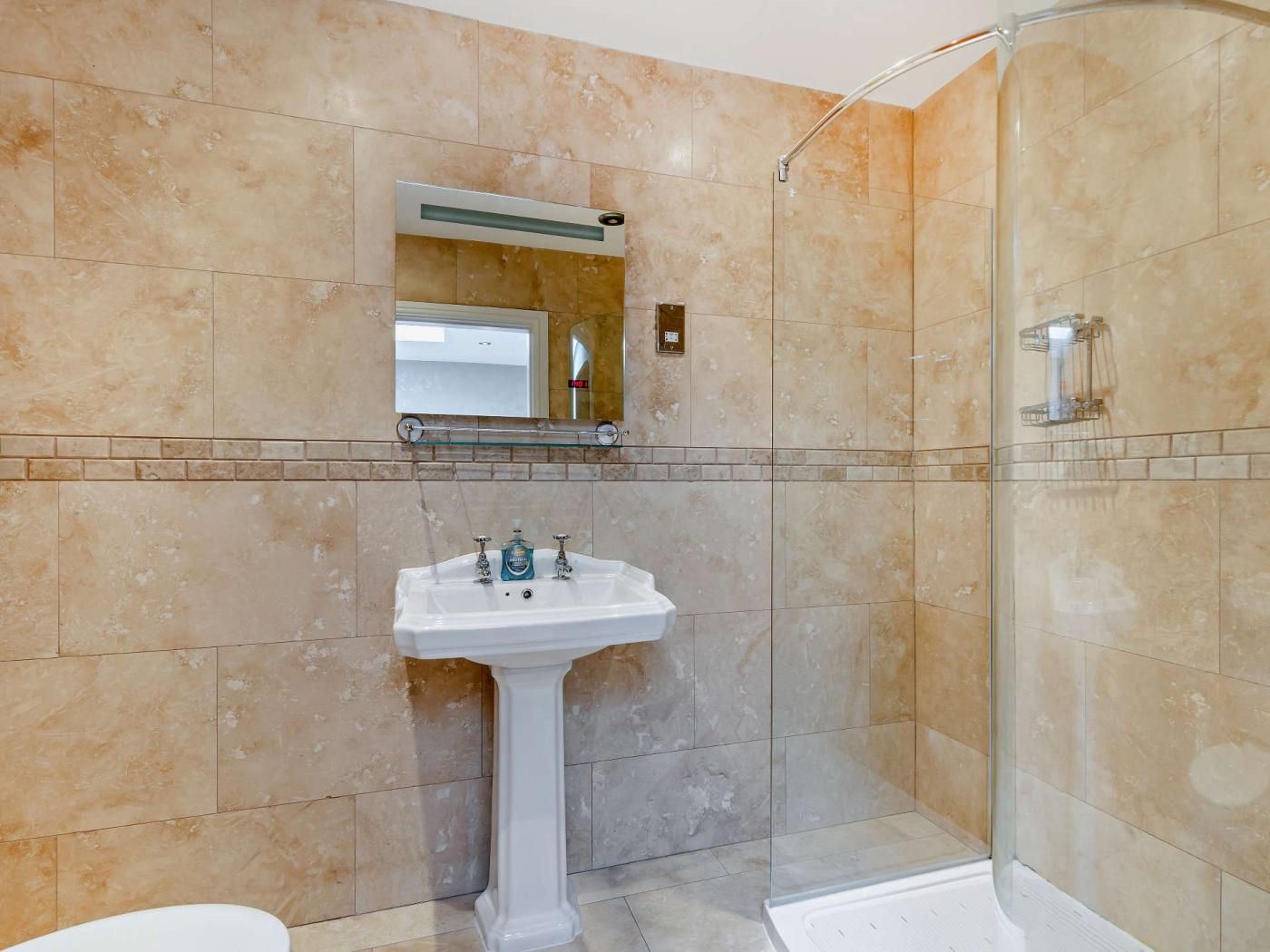 A bathroom with a pedestal sink, a glass shower enclosure, and a mirror above the sink.