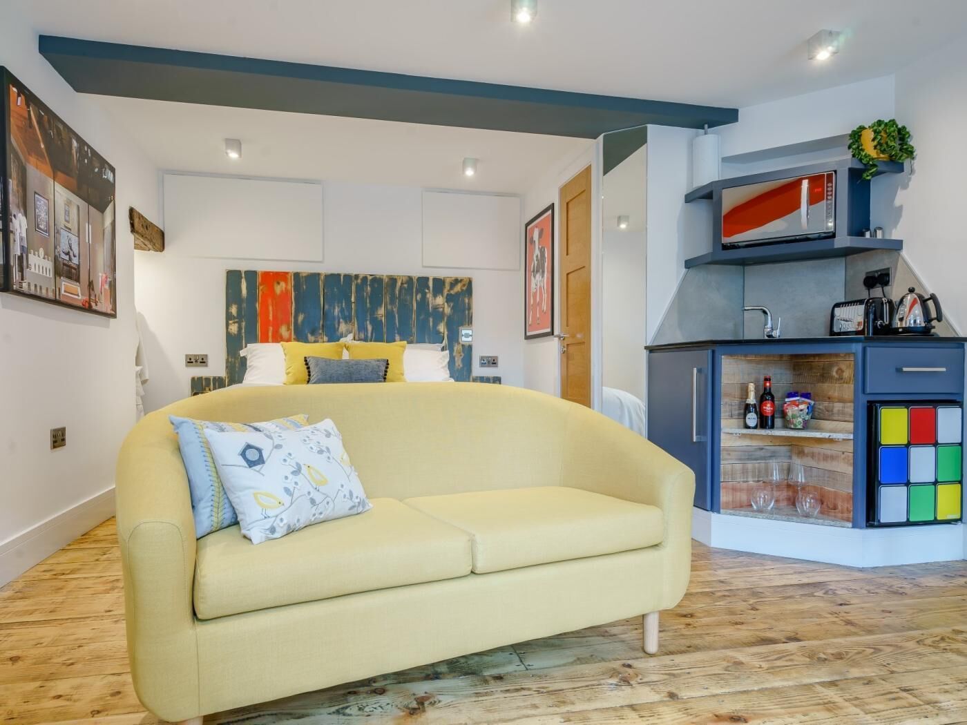 A modern living room with a sofa, a kitchen area with a microwave, and a dining table with glasses.