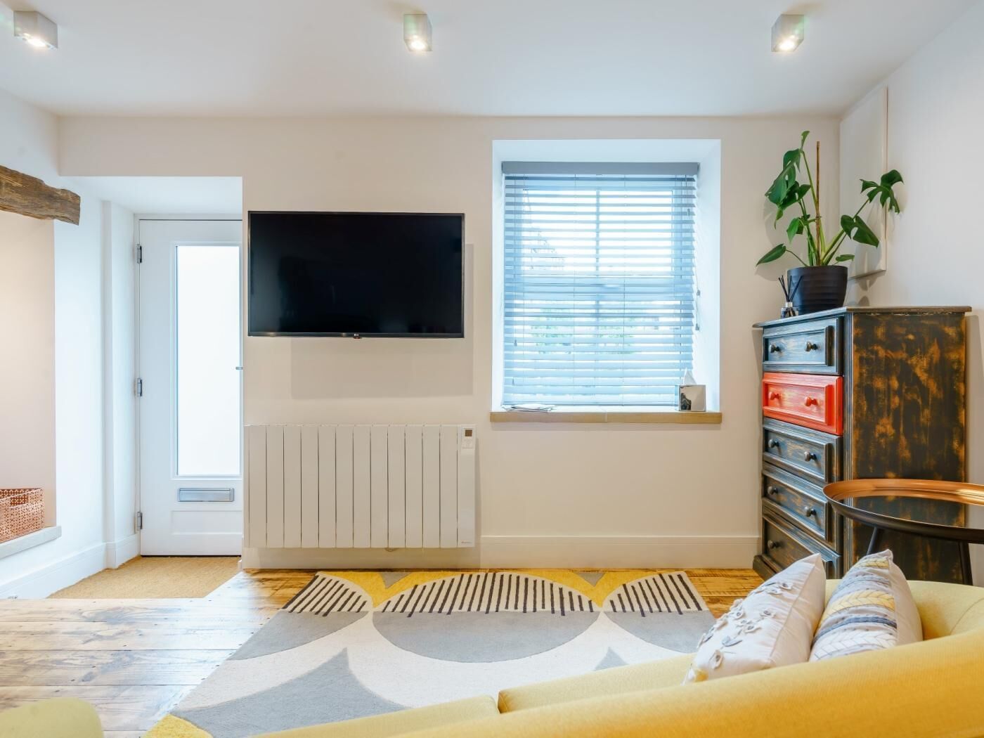 A living room with a sofa, a TV, a radiator, a window with blinds, and a cabinet.