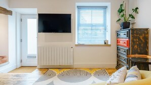 Un soggiorno con divano, televisore, termosifone, finestra con persiane e mobiletto.