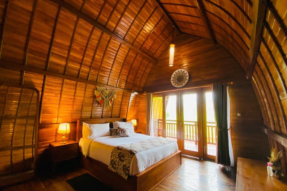 A wooden cabin bedroom with a bed, bedside tables, and a large window.
