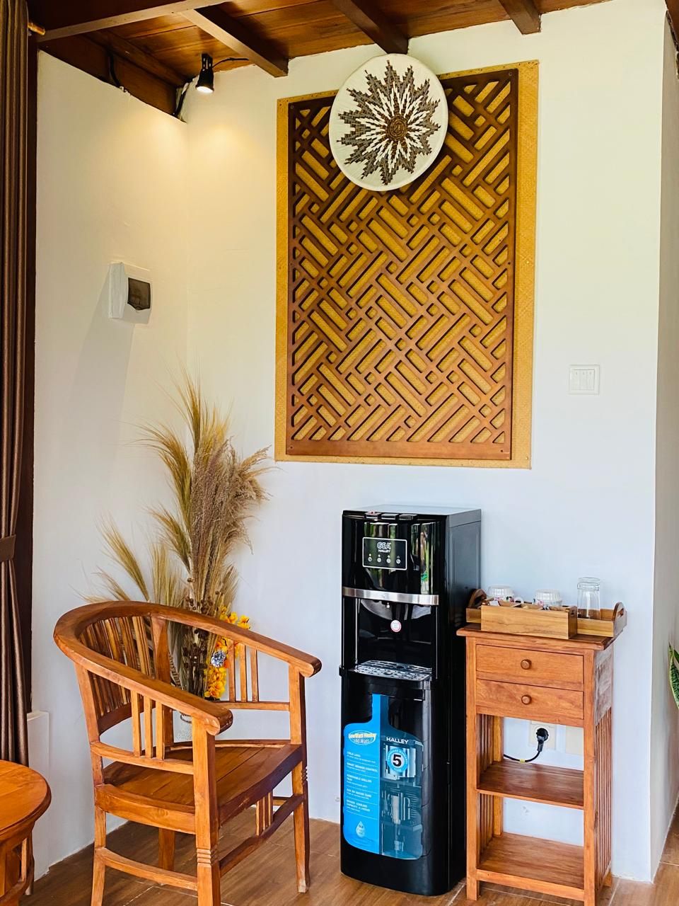 Habitación con panel de pared de madera, dispensador de agua, una silla de madera y una pequeña mesa de madera.