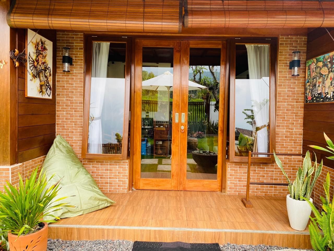 A wooden-framed entrance with glass doors, a brick wall, and potted plants.