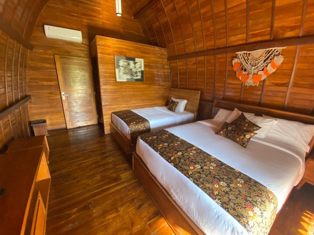 A room with two beds, wooden walls, a wooden floor, and a ceiling fan.