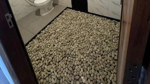 A bathroom with a marble wall, a white toilet, a shower, and a pebbled floor.