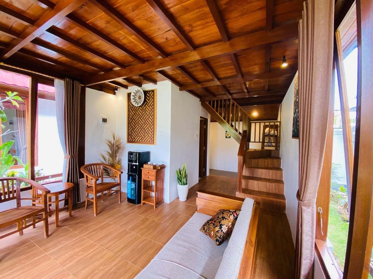 Ein Wohnbereich mit Holzboden, einer Couch, Sesseln, einer Kaffeemaschine und einer Treppe, die zu einer weiteren Ebene führt.