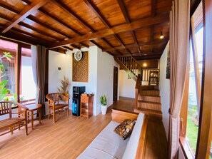 Ein Wohnbereich mit Holzboden, einer Couch, Sesseln, einer Kaffeemaschine und einer Treppe, die zu einer weiteren Ebene führt.