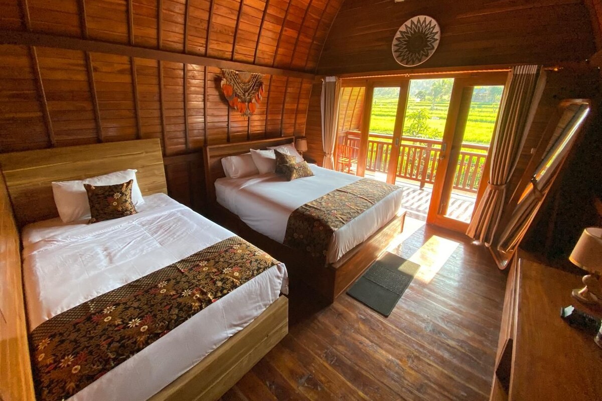 A wooden cabin with two beds, a balcony, and a view of a green landscape.
