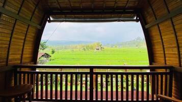 A wooden balcony with a view of a green field and a small house in the distance.