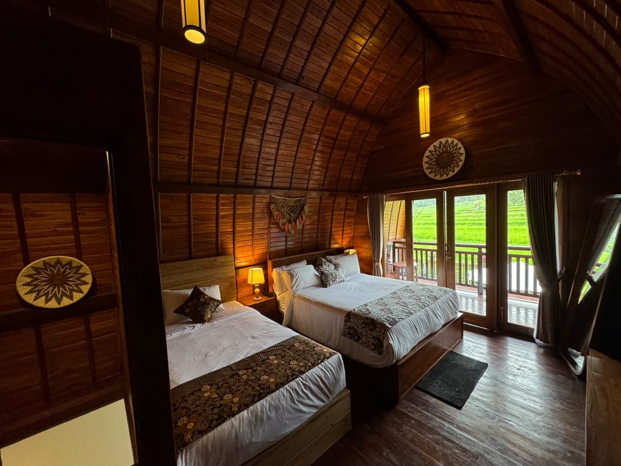 A room with two beds, wooden walls, a sloped ceiling, and a balcony with a view.