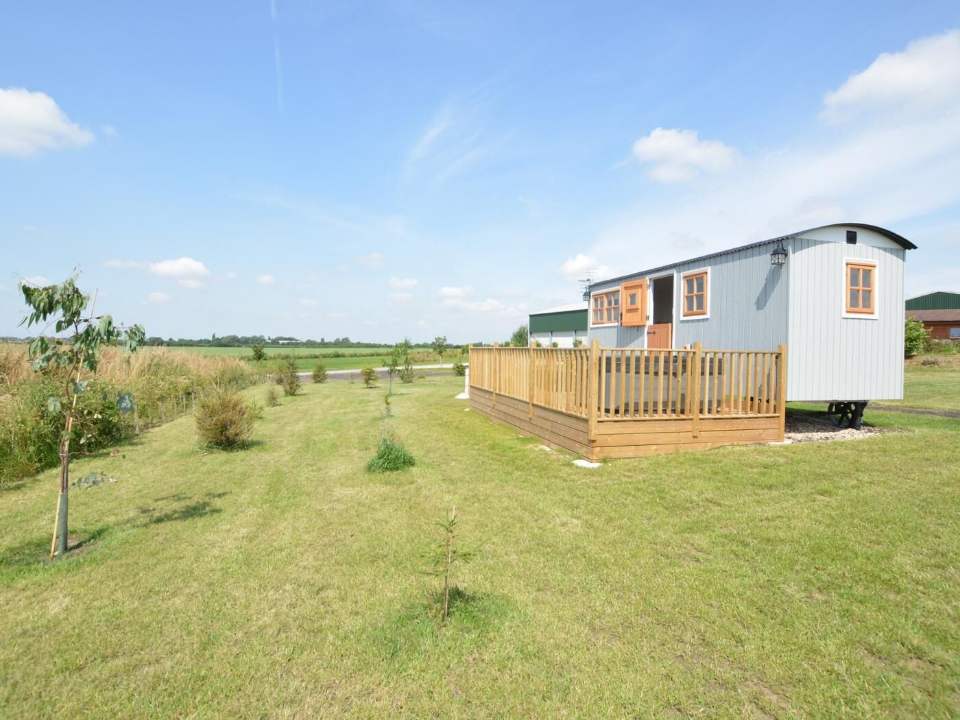 Une maison mobile de plain-pied avec une terrasse en bois, une cour clôturée et un ciel dégagé.